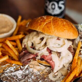 close up of pit beef sandwich with cheese sauce and sliced onions