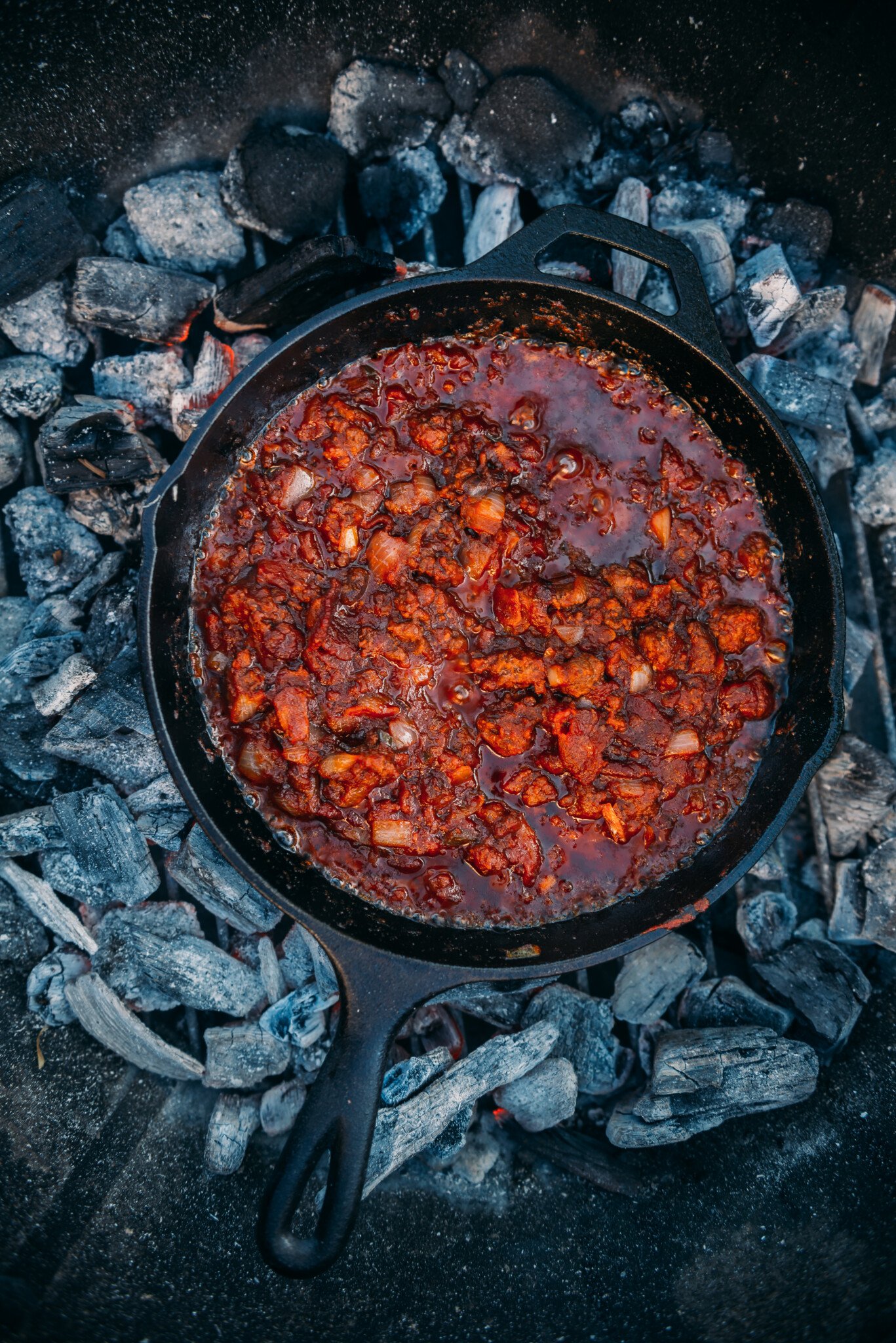 Cast iron skillet on coals filled with sloppy joe filling.