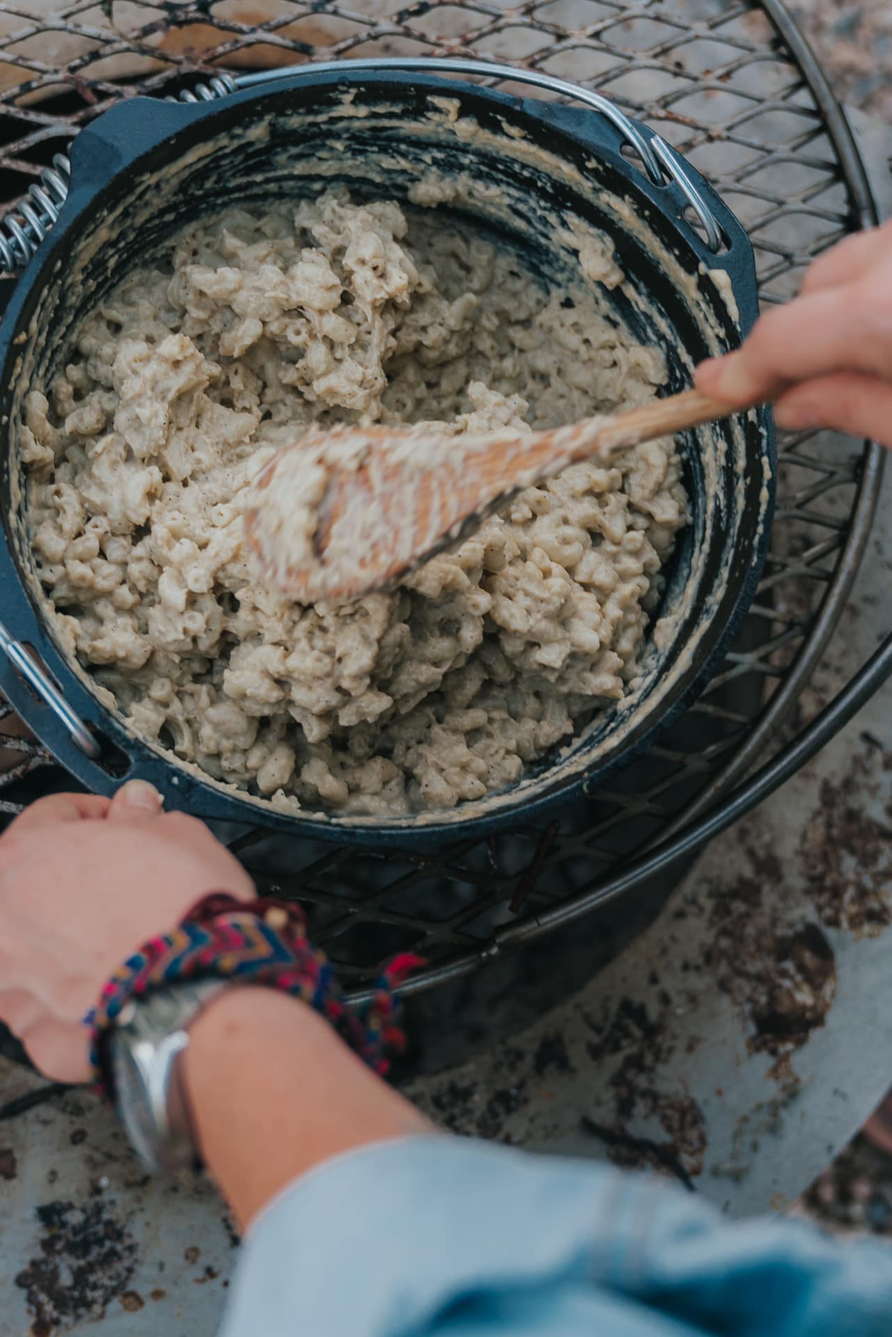 Hands stirring dutch oven filled with macaroni and cheese. 