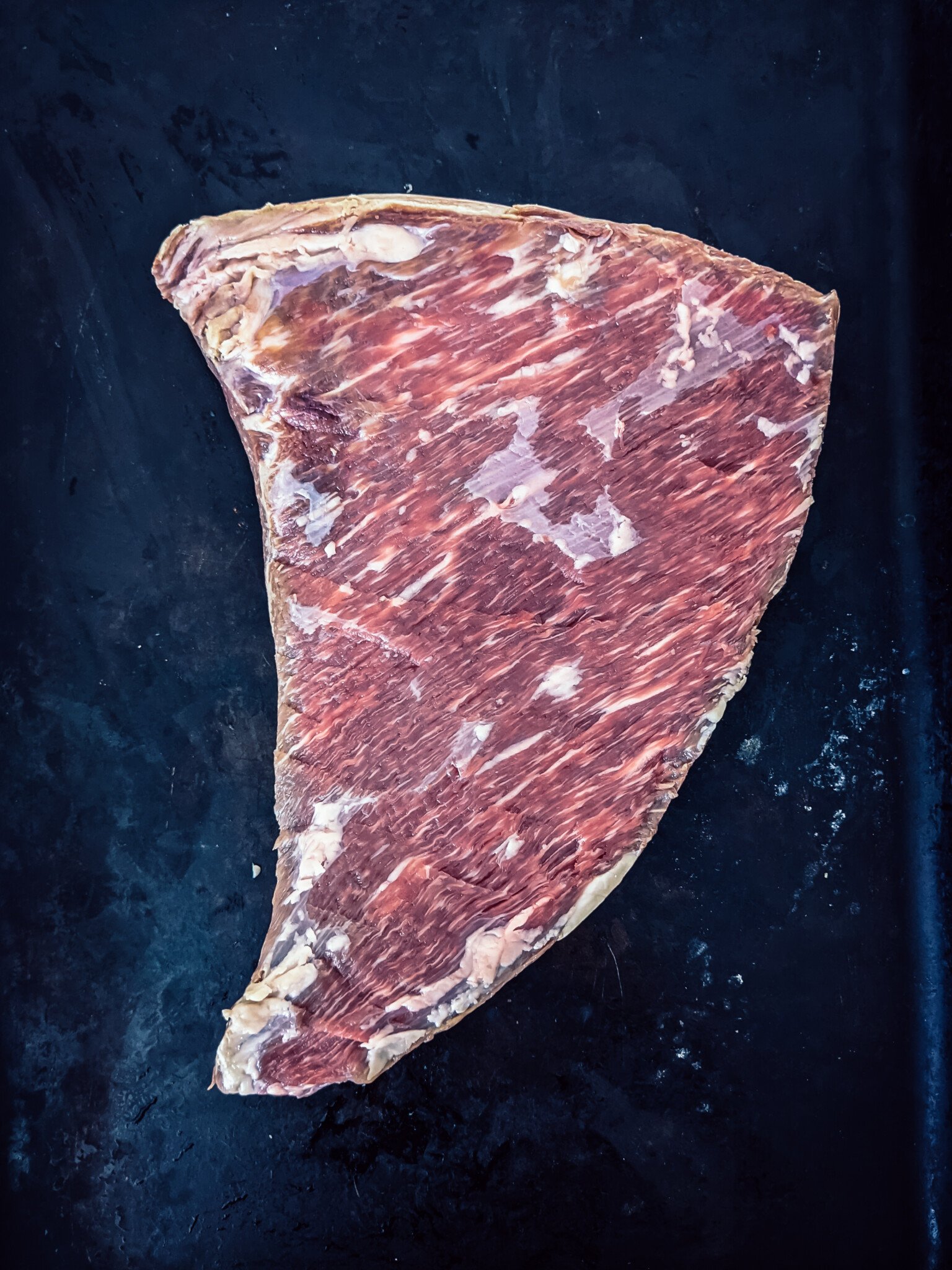 Raw tri-tip, silver skin removed, on a black board. 