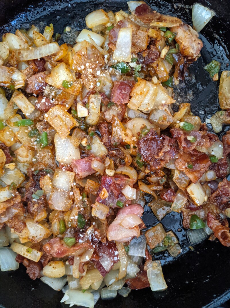 showing spices in skillet with sauteed veggies and bacon for sloppy joes