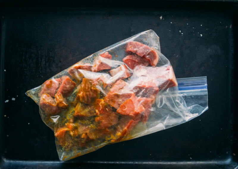 showing steak cut into cubes and marinating in resealable bag