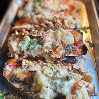 Lobster tails on a baking sheet with umami-rich cheese and herbs.