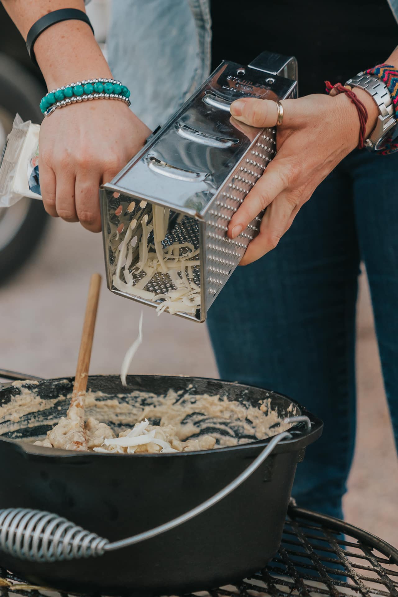 Hands holding cheese and a grater above a dutch oven.  