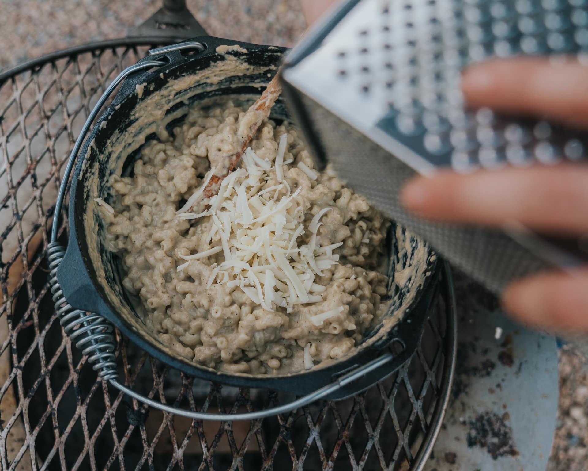 Dutch oven filled with macaroni and cheese being grated on top to melt. 