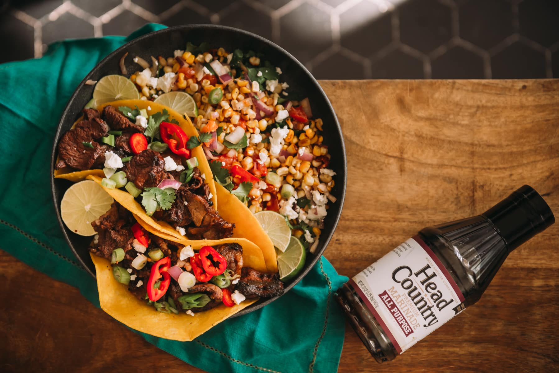 Above shot of platter with corn salsa and steak tacos topped with cilantro, cotija cheese and peppers. Bottle of Head country marinade on the side (as it was the marinade for the recipe) 