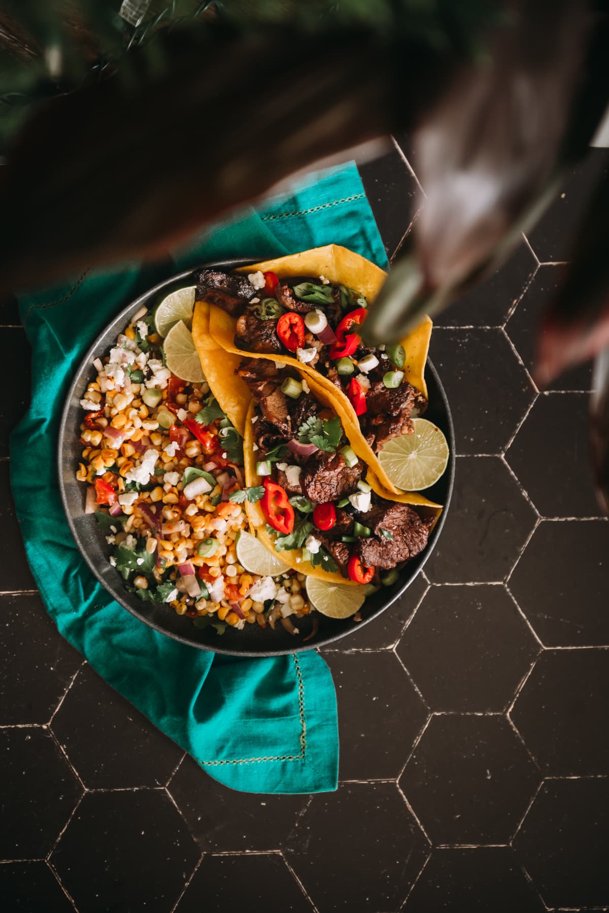 Overhead shot of colourful grilled steak tacos with cilantro, scallions, cilantro, peppers and corn salsa on the side. 