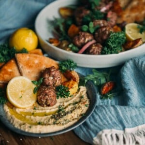 lamb meatballs on a plate with hummus and pita, lemon wedges and herbs for garnish