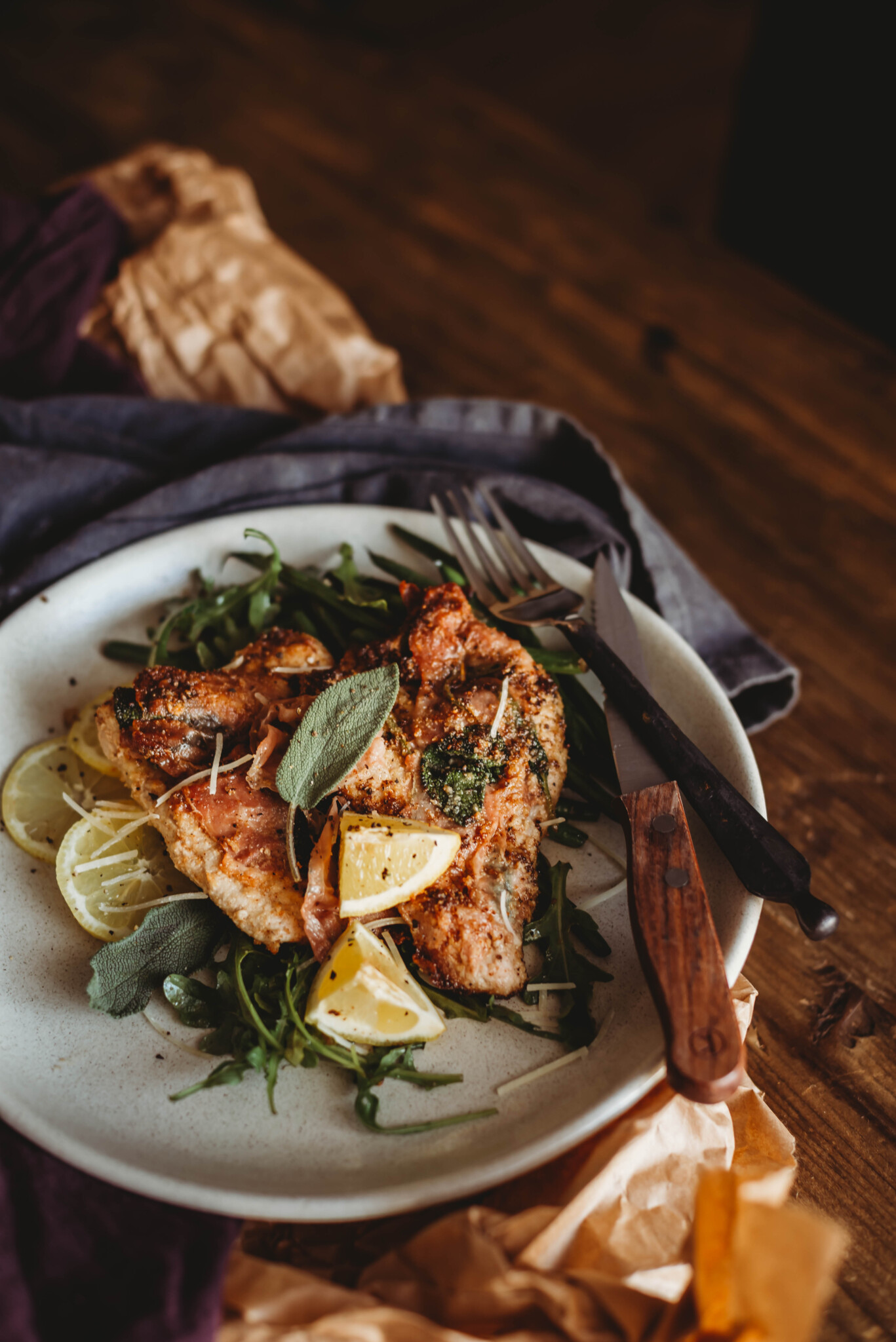 veal saltimbocca on a plate with arugula and lemons