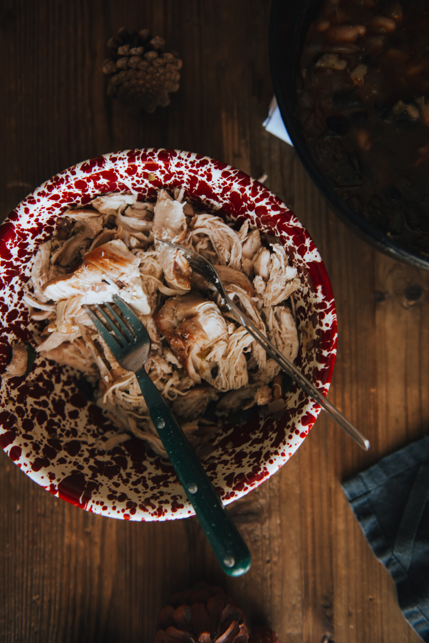 Showing chicken being pulled with forks in a red speckled bowl 