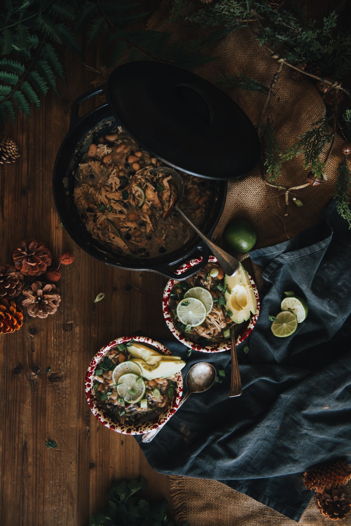 Above shot showing white chicken chili in a dutch oven with two bowls assembled near by topped with avocado and lime.