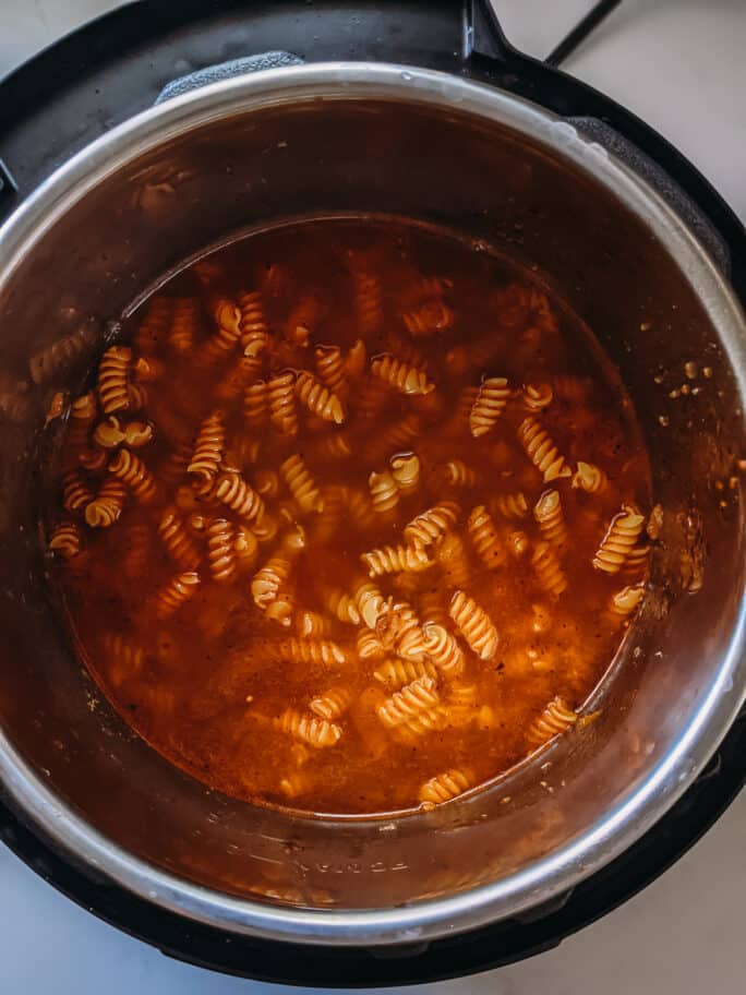 instant pot with dried pasta and broth ready to cook