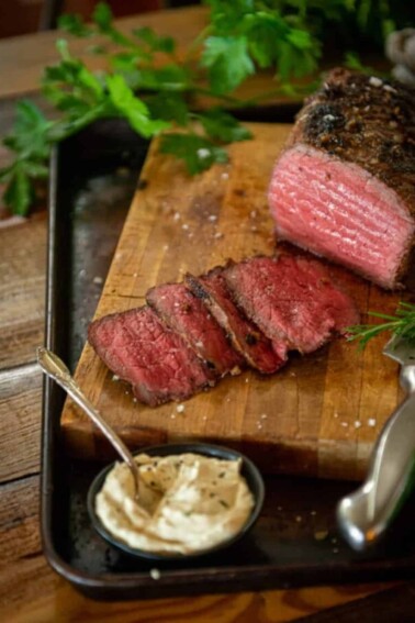Medium rare smoked roast beef on a wooden cutting board with a side of horseradish sauce.