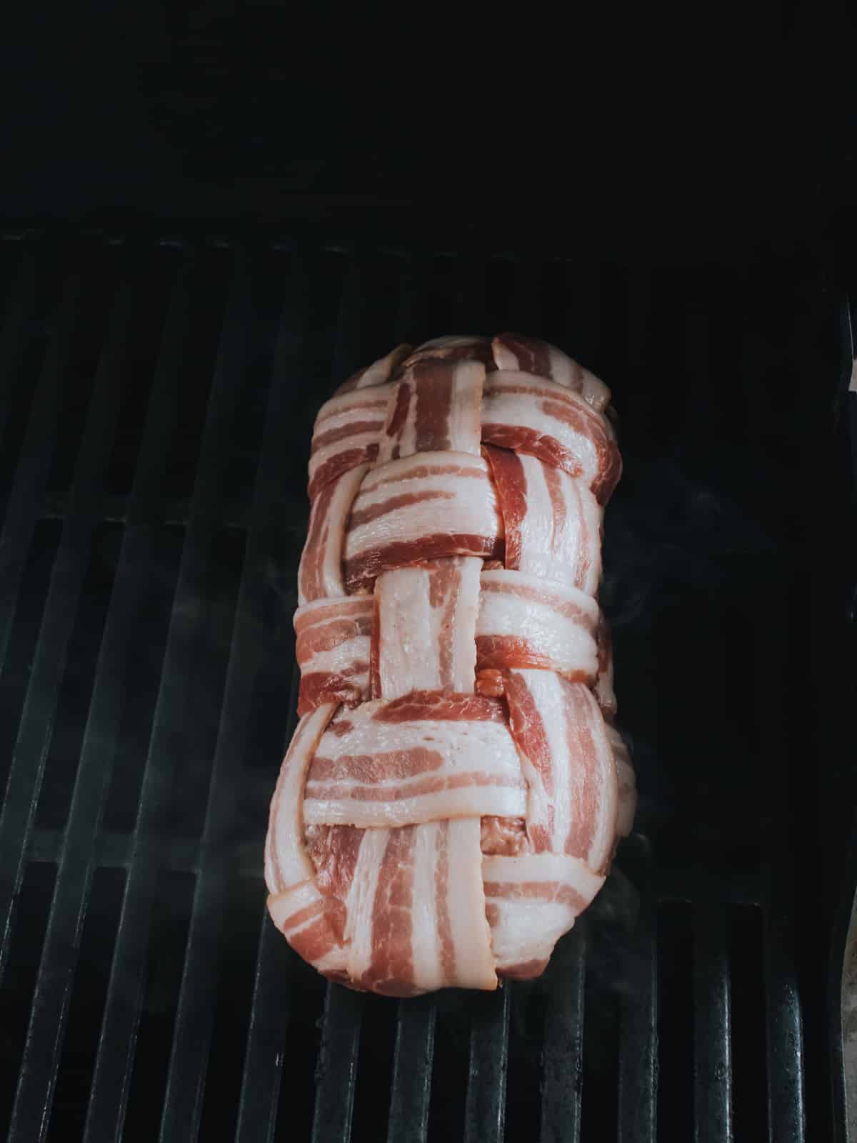 placing loaf of sausage wrapped in bacon on grill