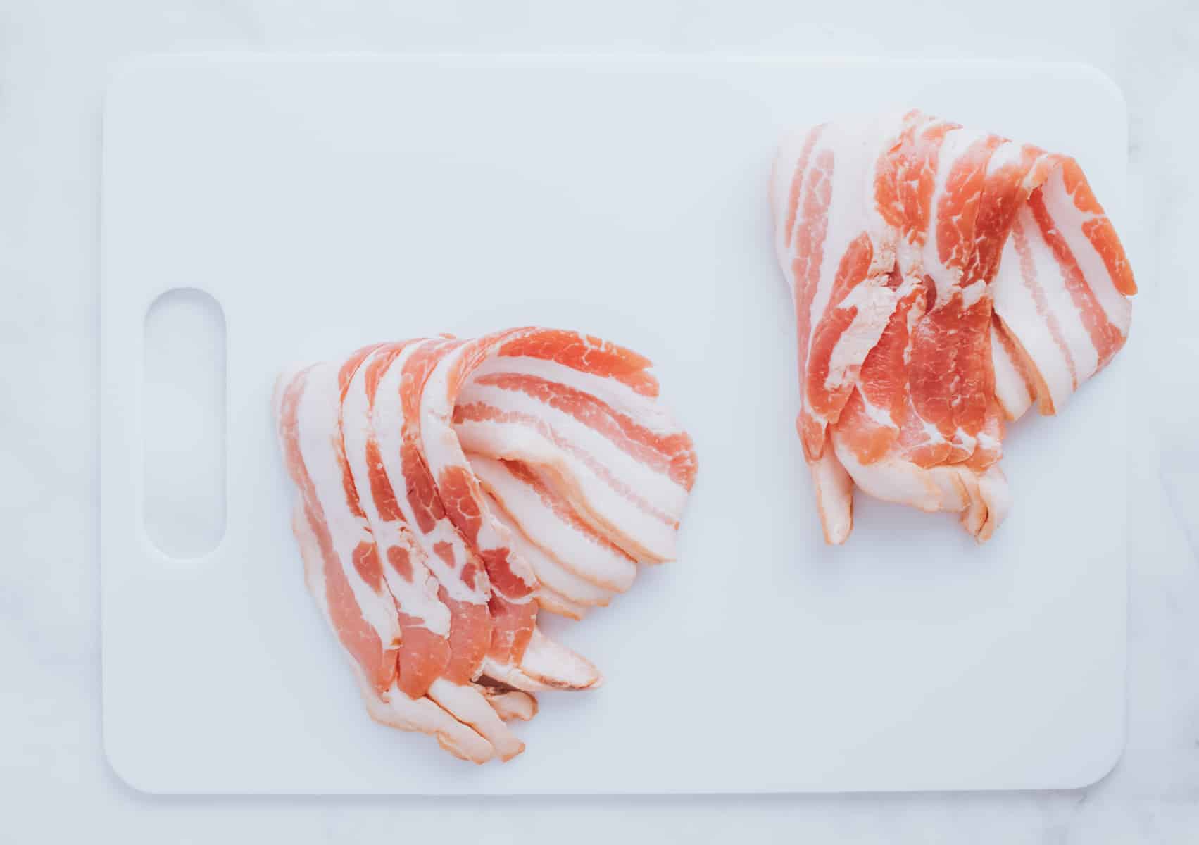 two piles of uncooked bacon on a cutting board