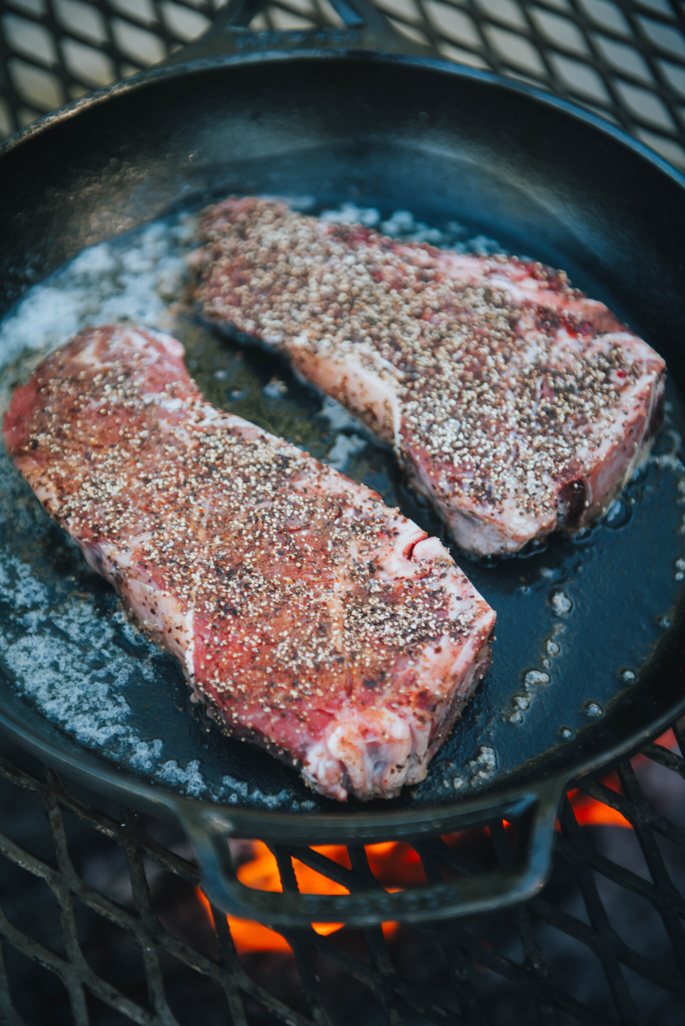 Steaks in hot skillet over campfire.
