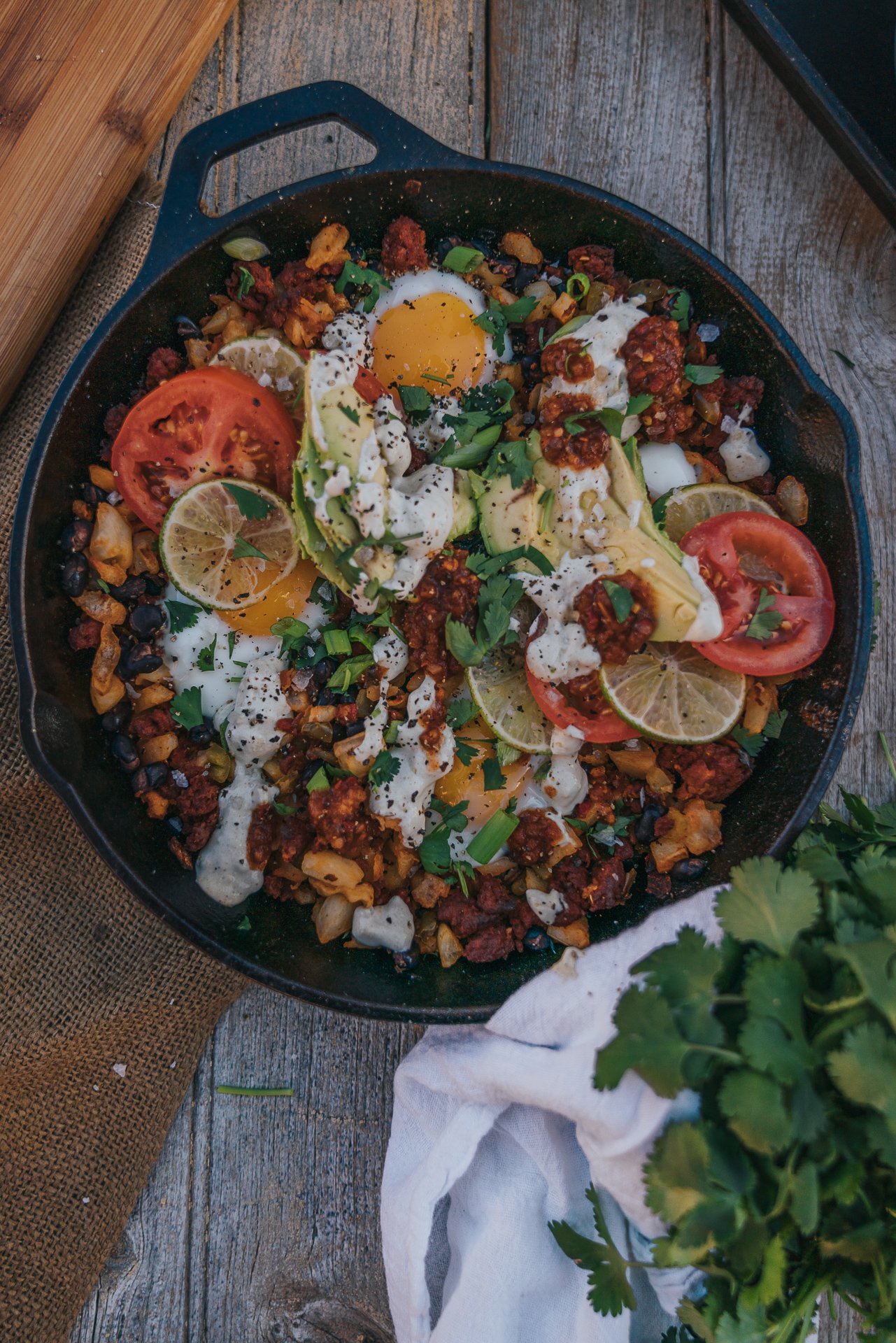 overhead shot of colorful cast iron skillet of fried eggs, potato chorizo hash and toppings. 