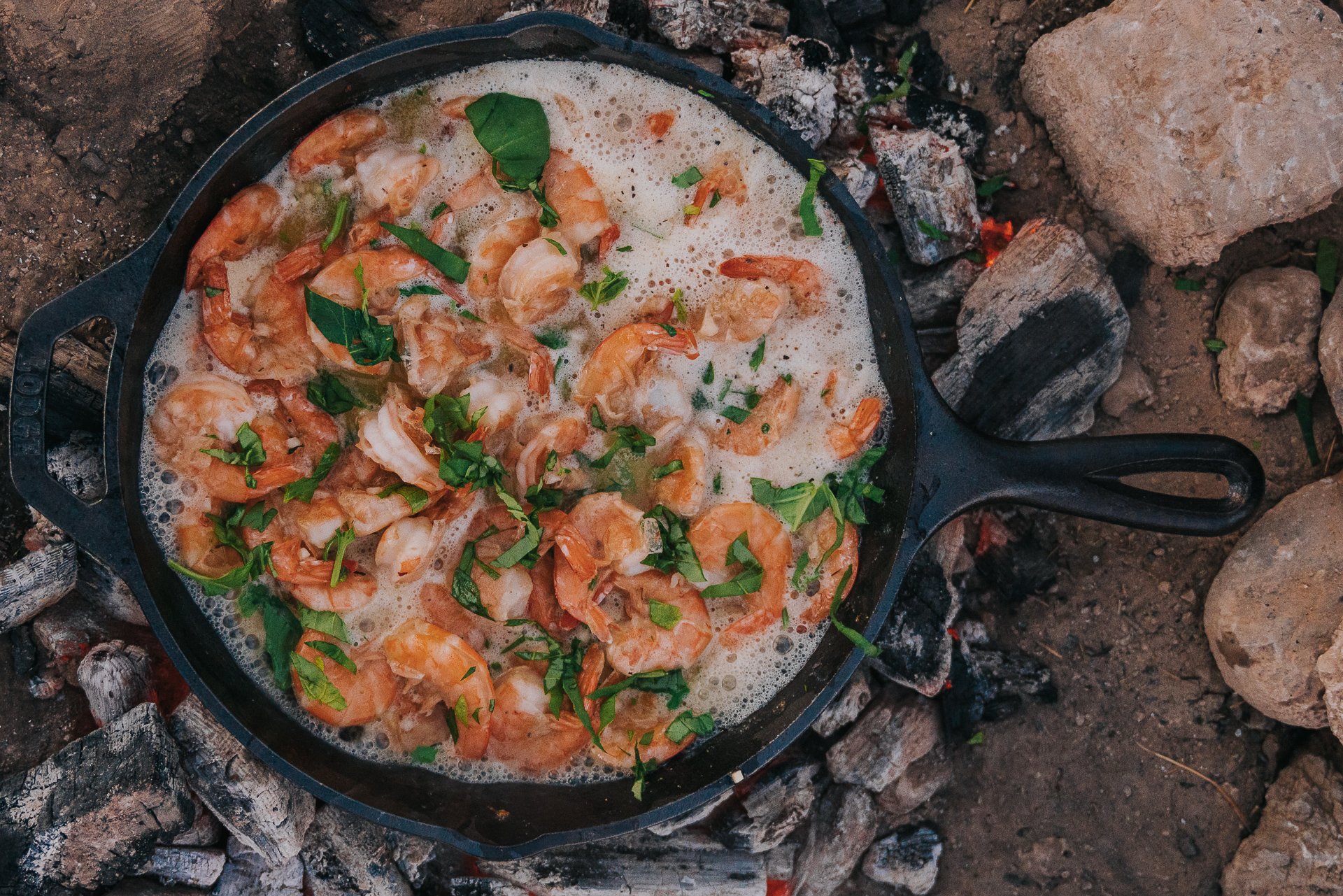 overheat shot of a cast iron skillet filled with large shrimp in a buttery garlic sauce garnished with fresh herbs. 
