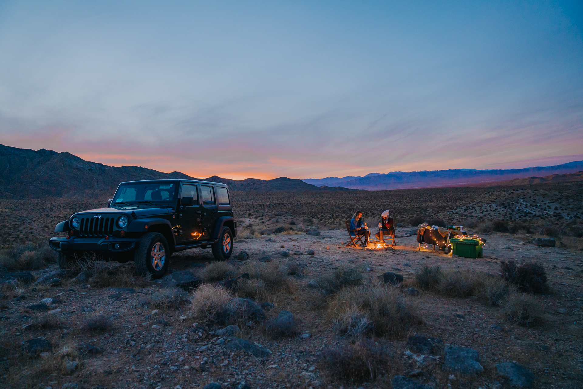 camp scene with jeep and friends eating dinner around a campfire 