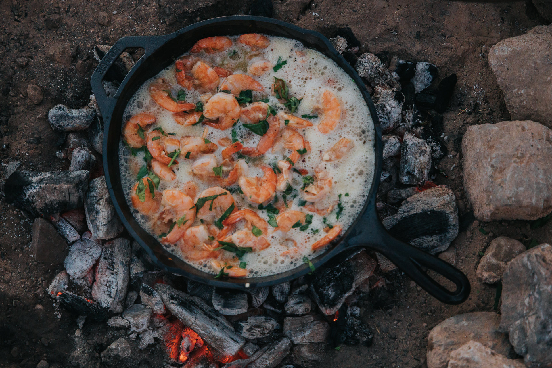 Cast iron skillet over a campfire filled with garlic butter shrimp
