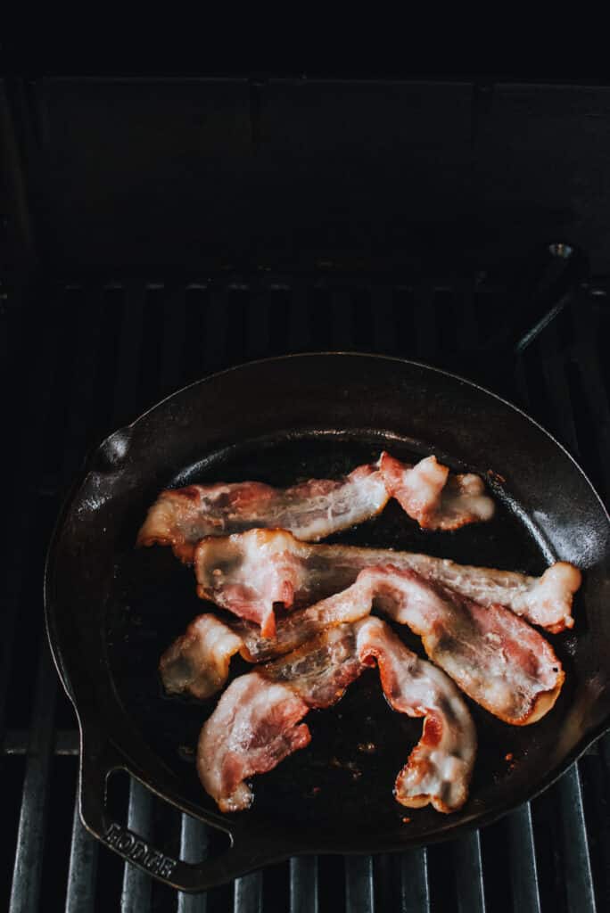 cooking bacon in a cast iron skillet on the grill