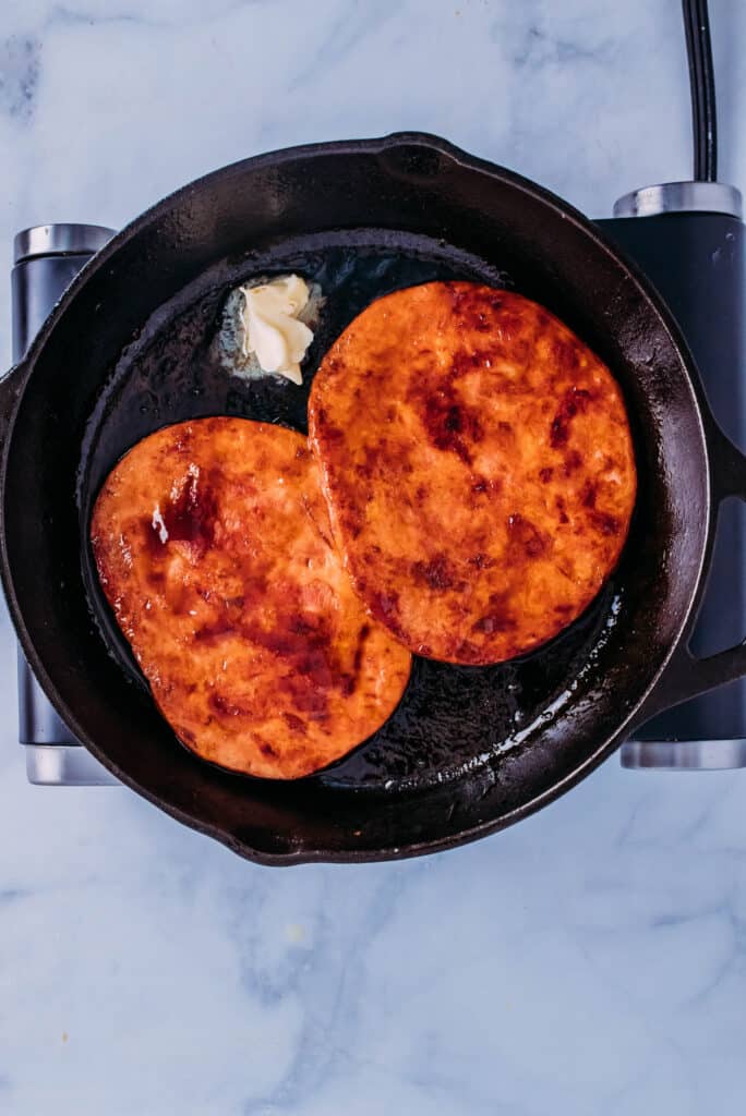 Ham steaks frying in the skillet with butter.