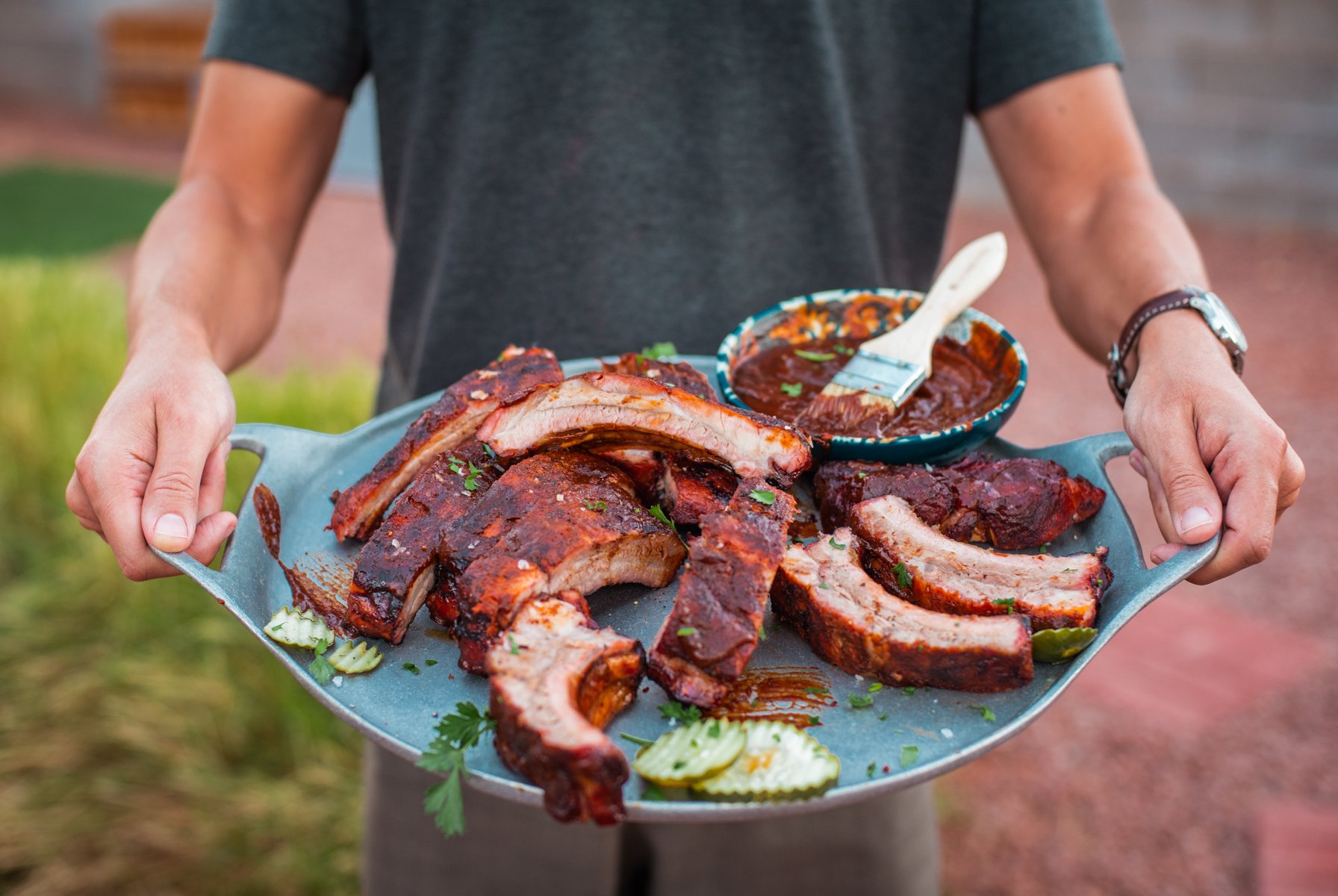 smoked ribs sliced and being held on a platter by particularly strong and handsome arms