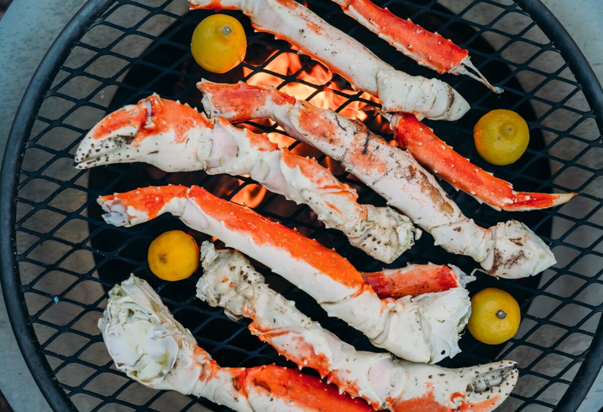 Crab legs over on a grill grate over a fire pit. 
