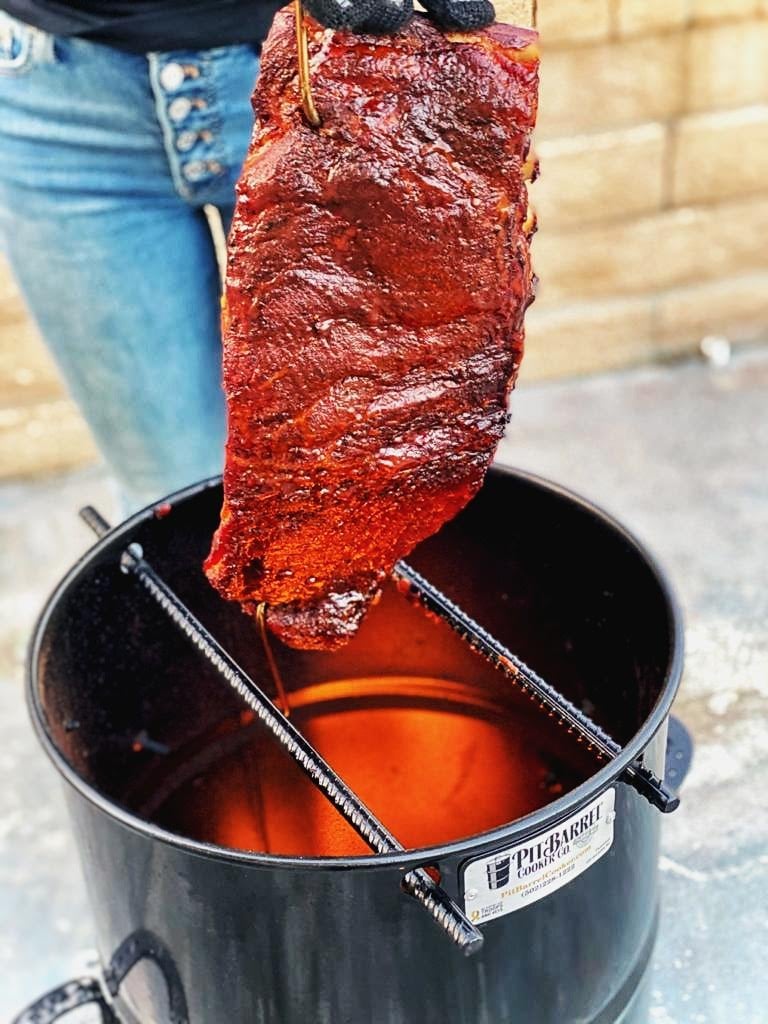 Glistening smoked rib rack being pulled from a smoker. 