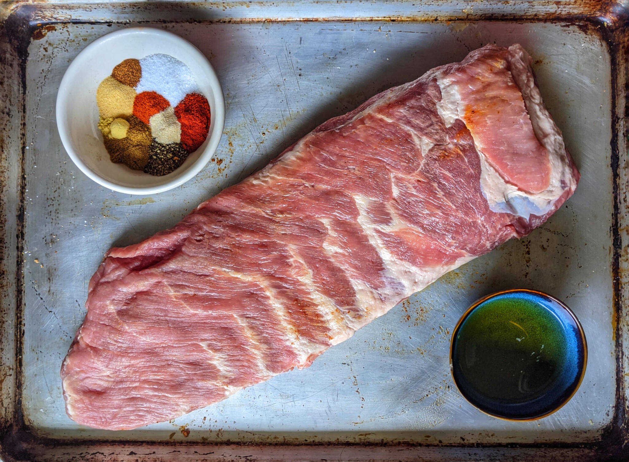 Raw rack of ribs on a tray with spices in a bowl ready to be seasoned. 