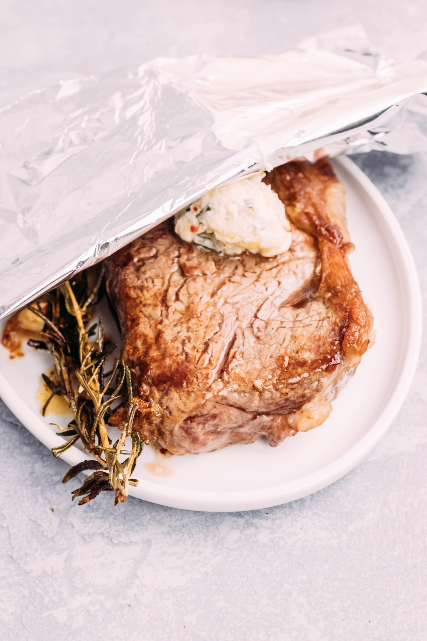 Close up of steak topped with butter, tented with foil to rest.