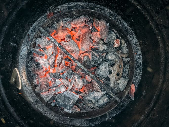 Glowing embers of ashed over charcoal in the bottom of a grill. 