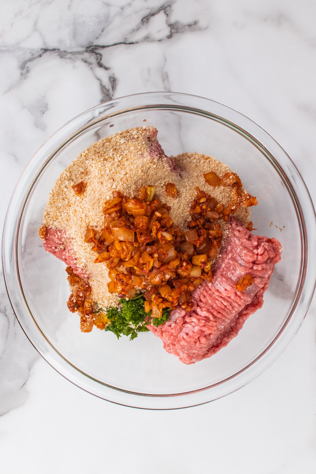 Ground meat, onions, breadcrumbs and other ingredients for meatloaf in a bowl.