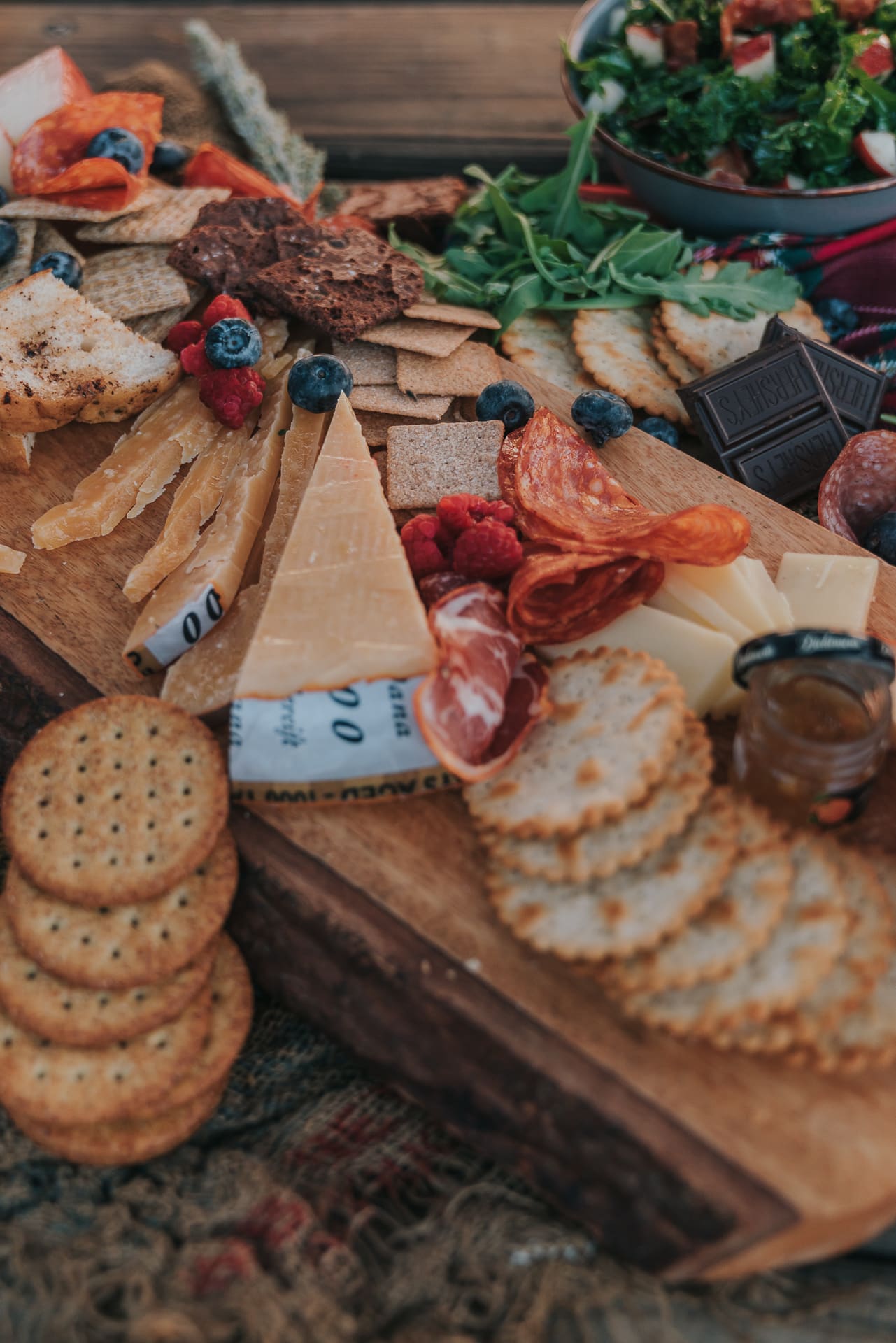 Wooden board with cured meats, crackers, and cheese.