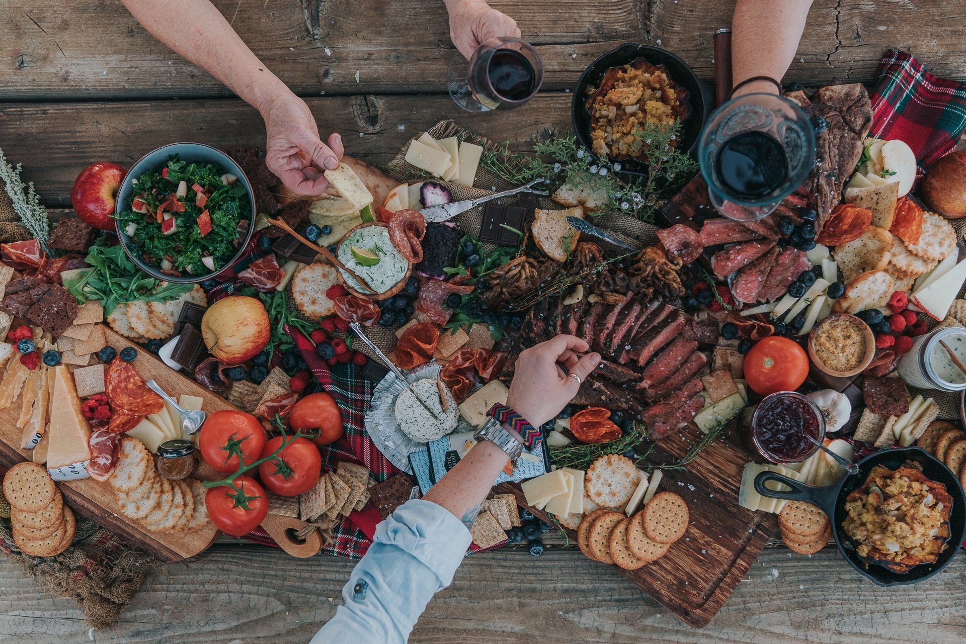 Overhead shot of rustic table and charcuterie board with hands reaching in.
