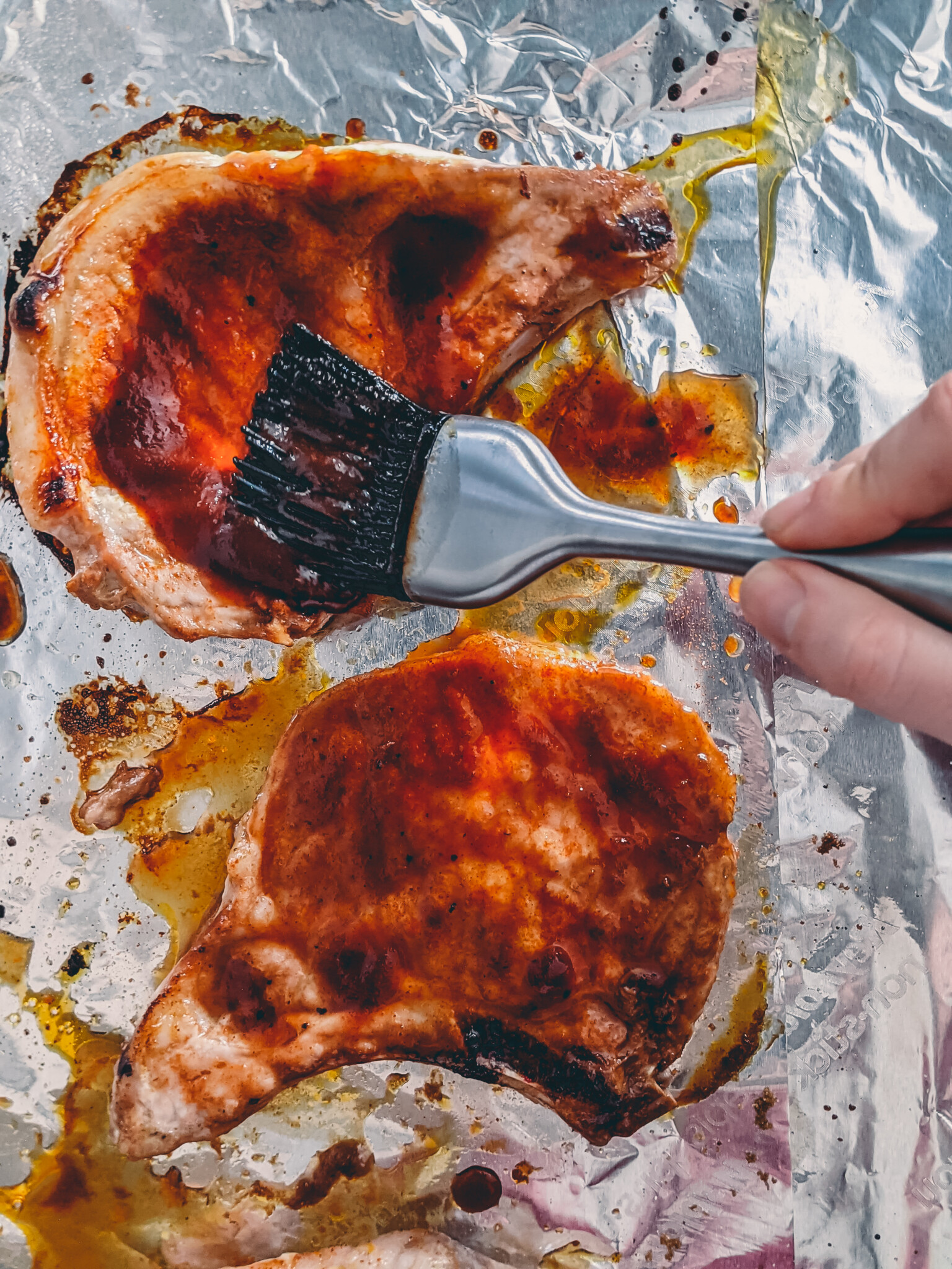 Hand brushing pork chops with bbq sauce. 