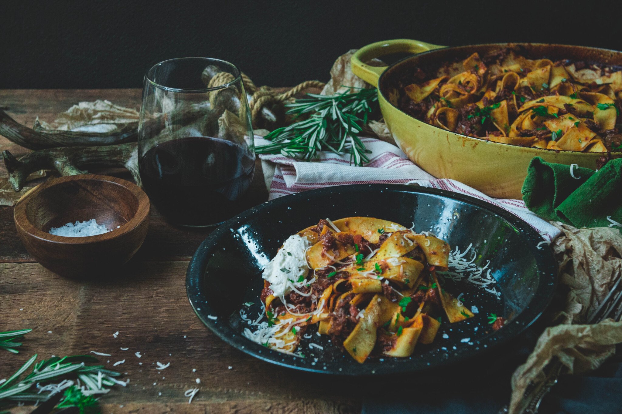 A black plate with shredded beef cheek ragu recipe with pasta and garnished with ricotta and herbs 