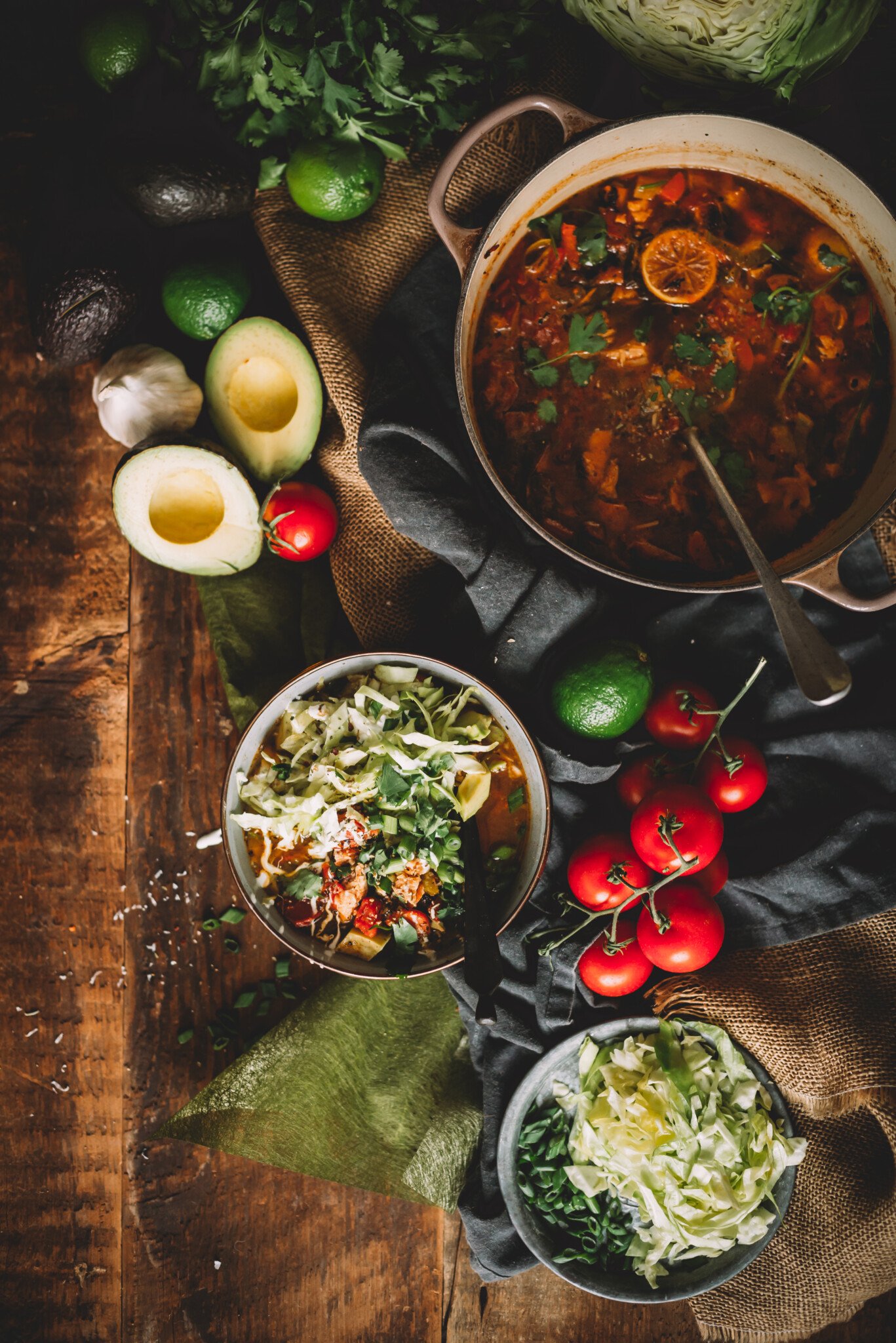 Overhead shot of bowls of Mexican chicken soup with shredded cabbage, scallions, cilantro as garnish and a Dutch oven of soup in the frame