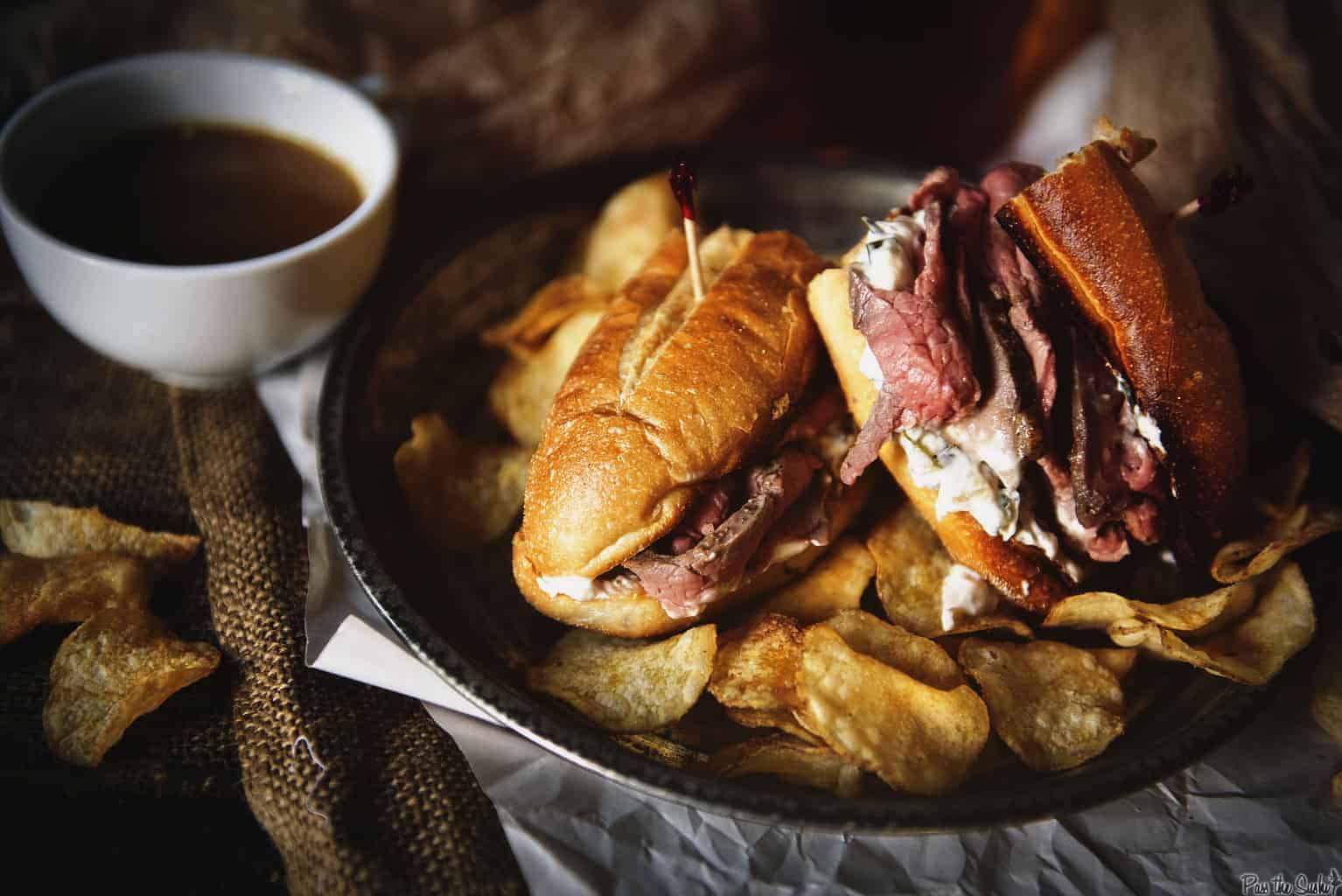 Tender sliced beef and onion spread in a toasted french roll on a platter with chips.