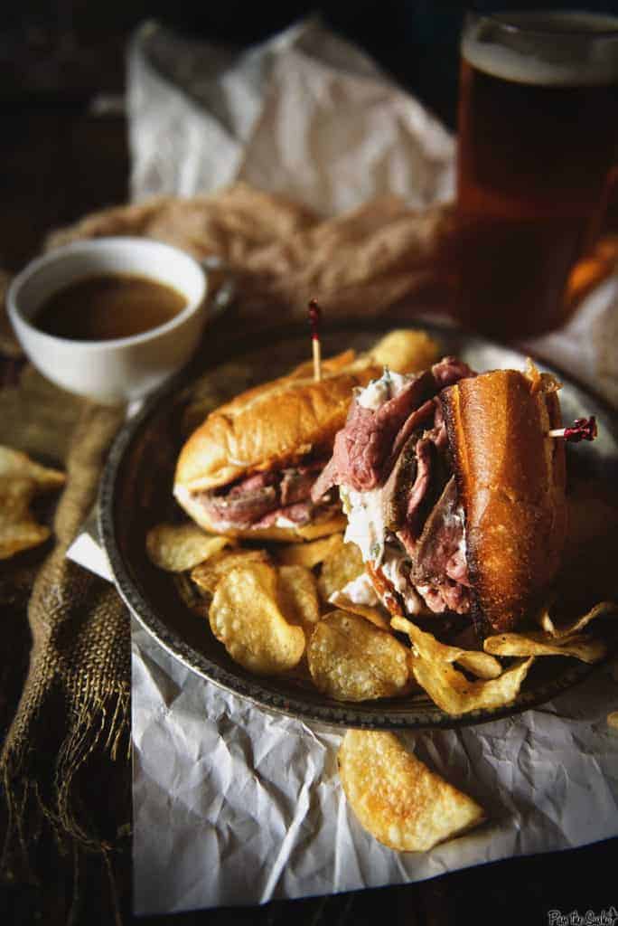 French dip sandwich with toasted roll on a platter with chips an au jus. 
