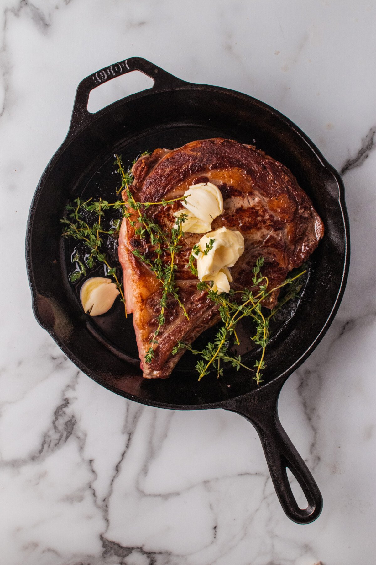 Garlic and herbs added to a skillet over a steak. 