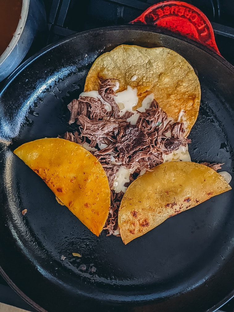 Birria tacos being assembled in a pan for frying.