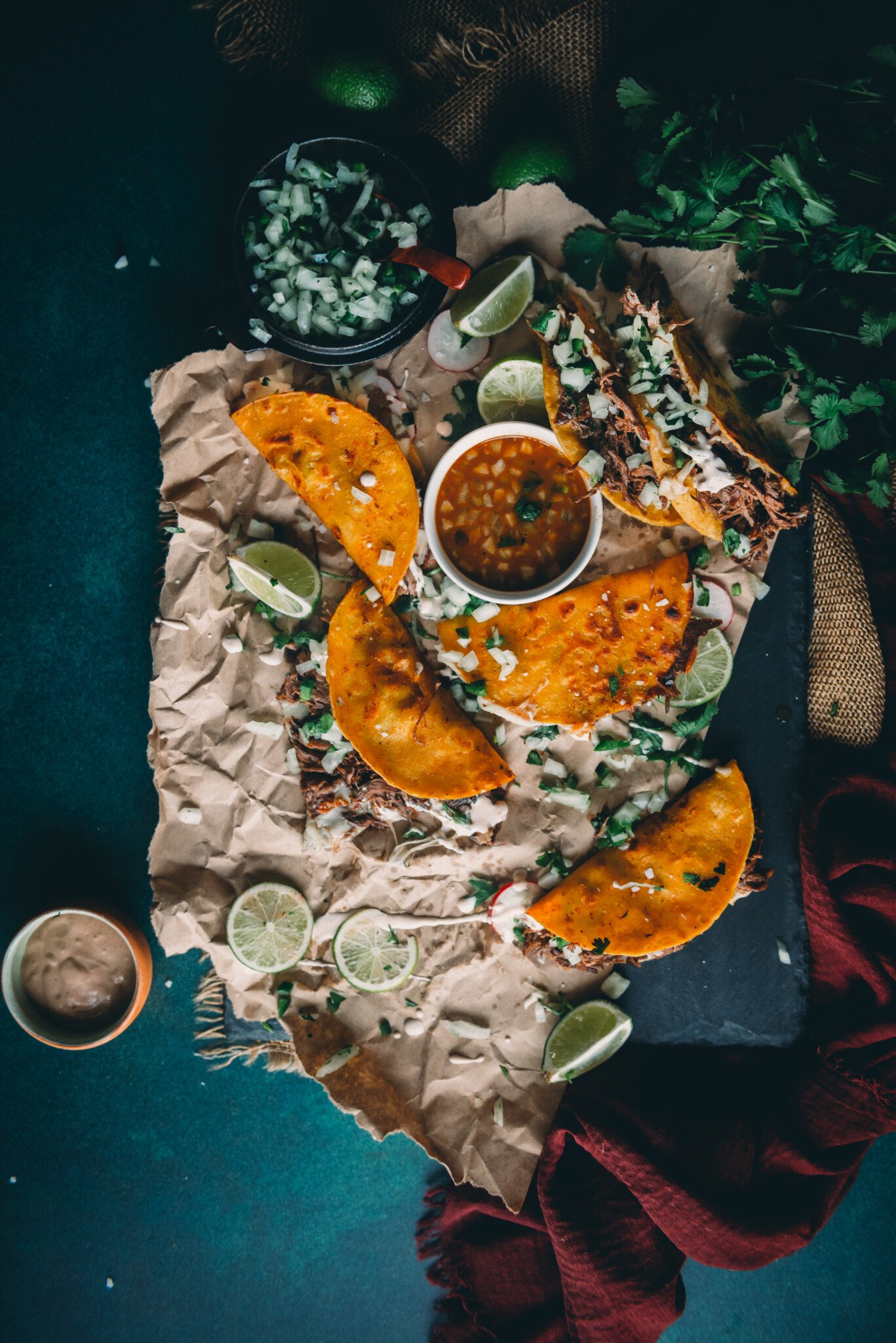 Overhead shot of platter with messy quesabirria tacos on paper. 