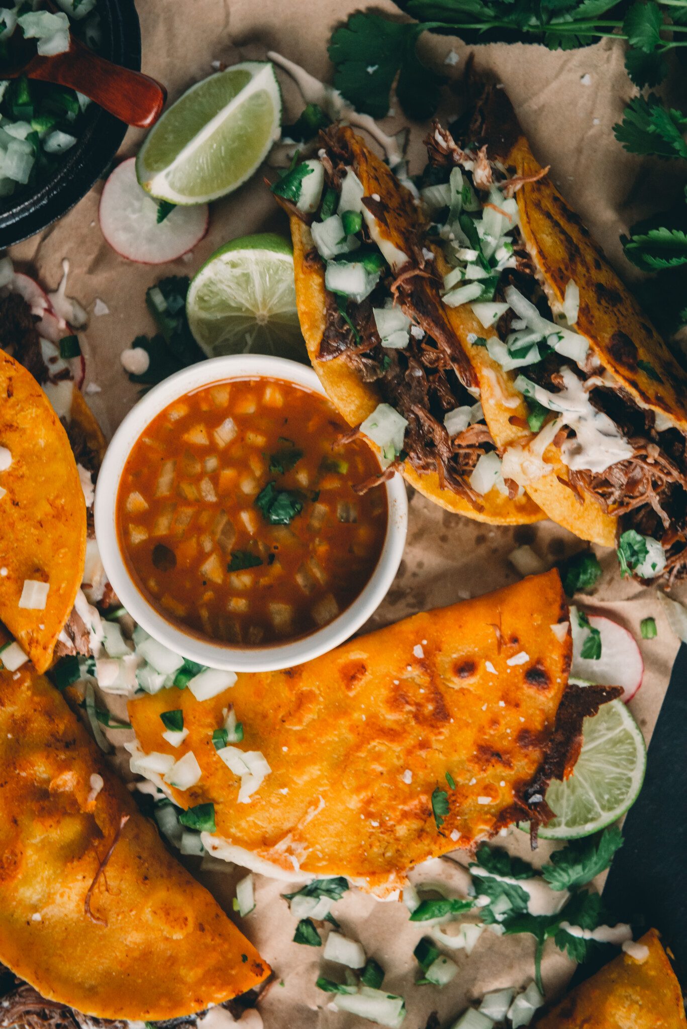 Overhead shot of quesabirria tacos with consommé on table.