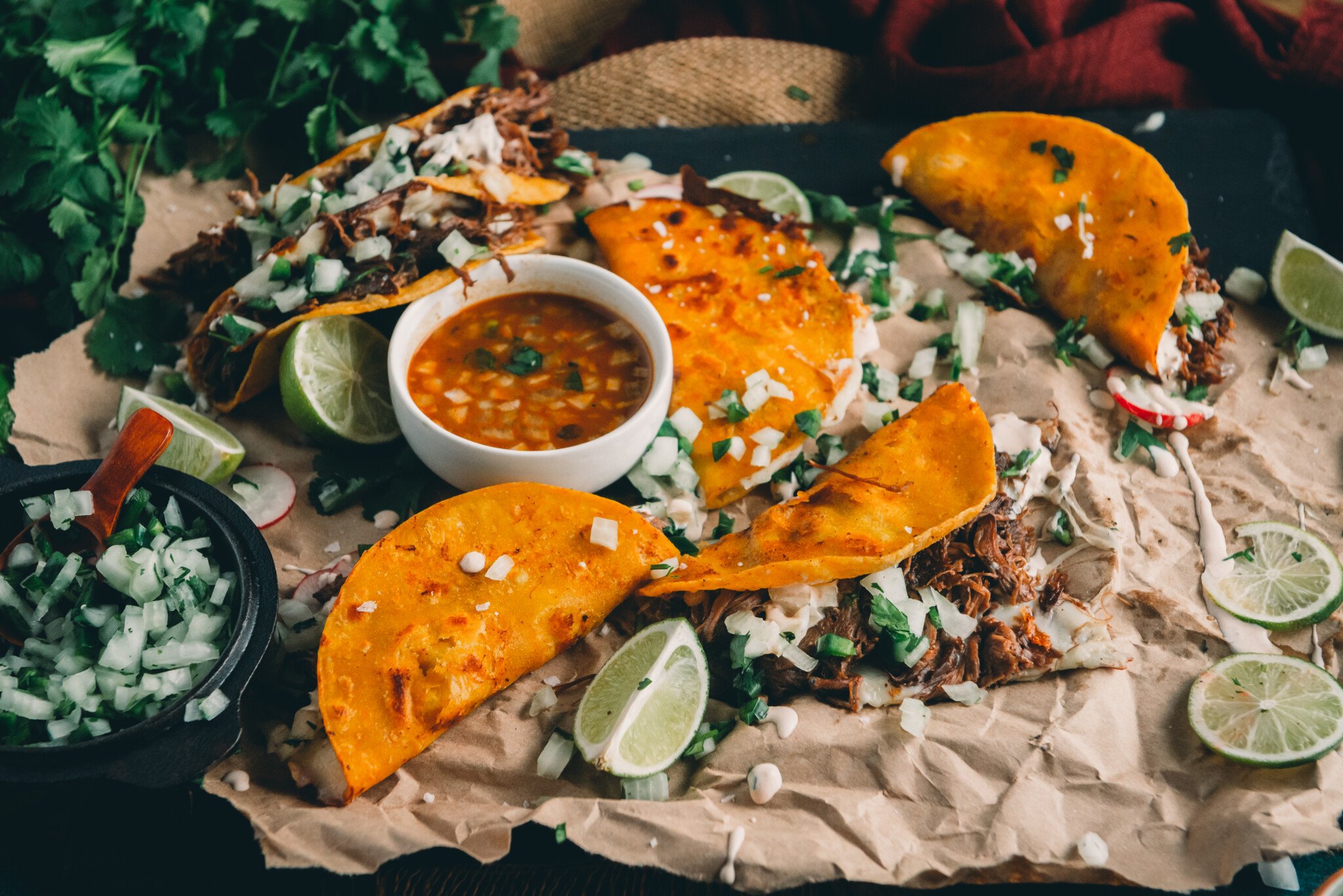 Rustic platter with quesabirria, limes, and cilantro onion garnish.