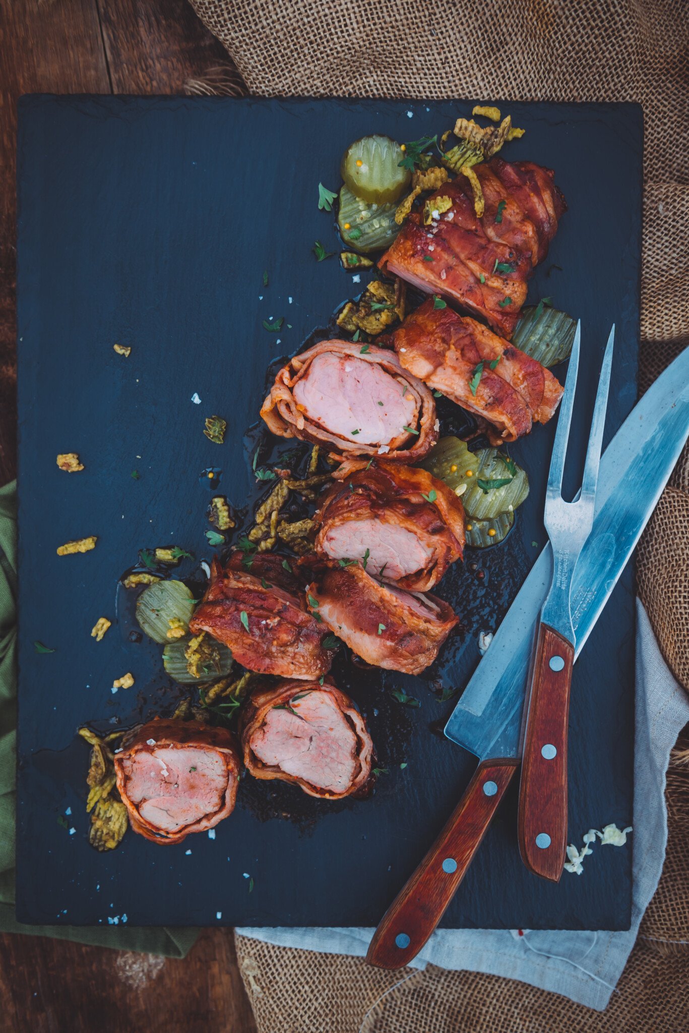 Overhead shot of cutting board with smoker pork tenderloin on it wrapped in bacon.