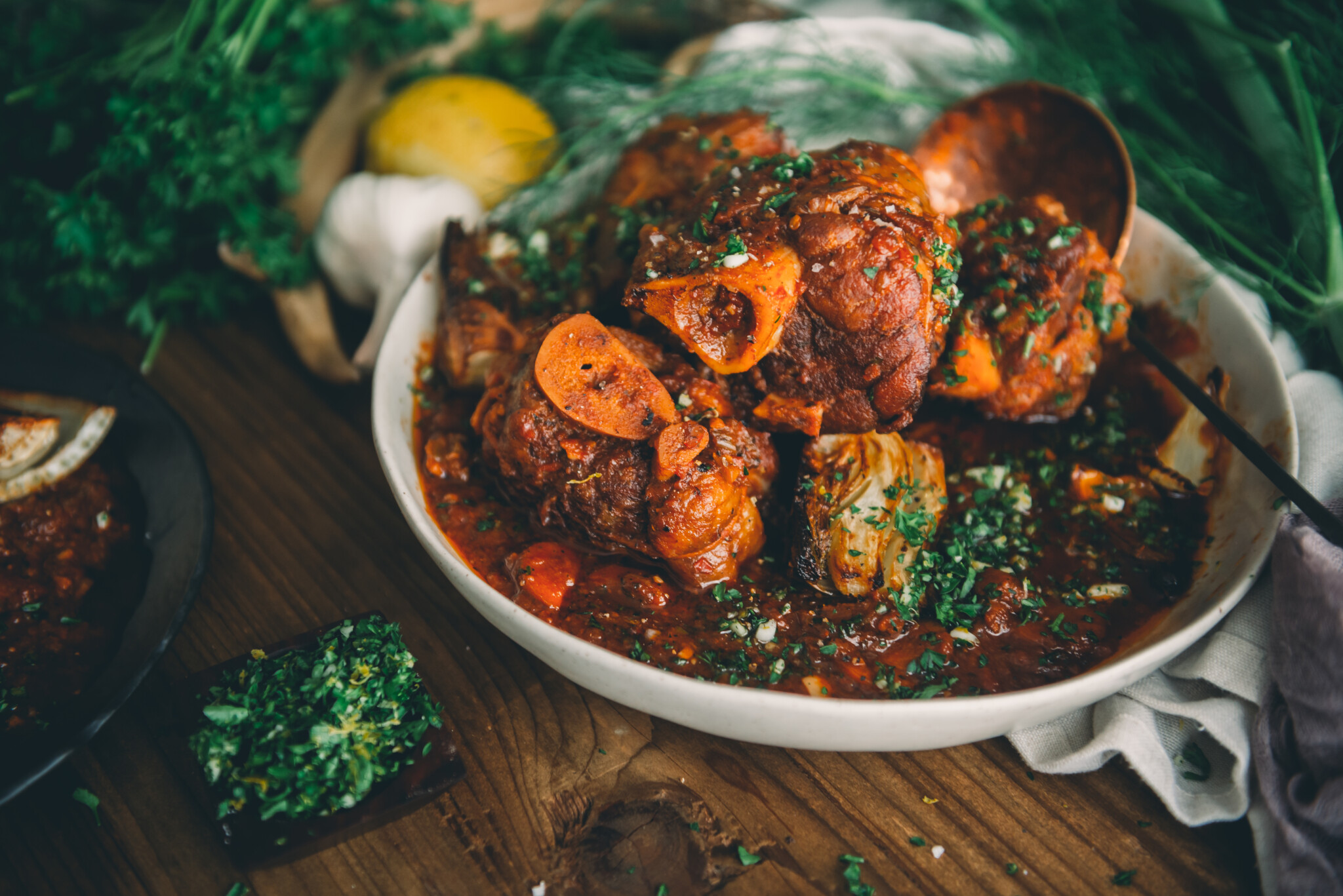 Platter of sous video osso buco pork shanks with roasted fennel in sauce with garnish of gremolata near by.