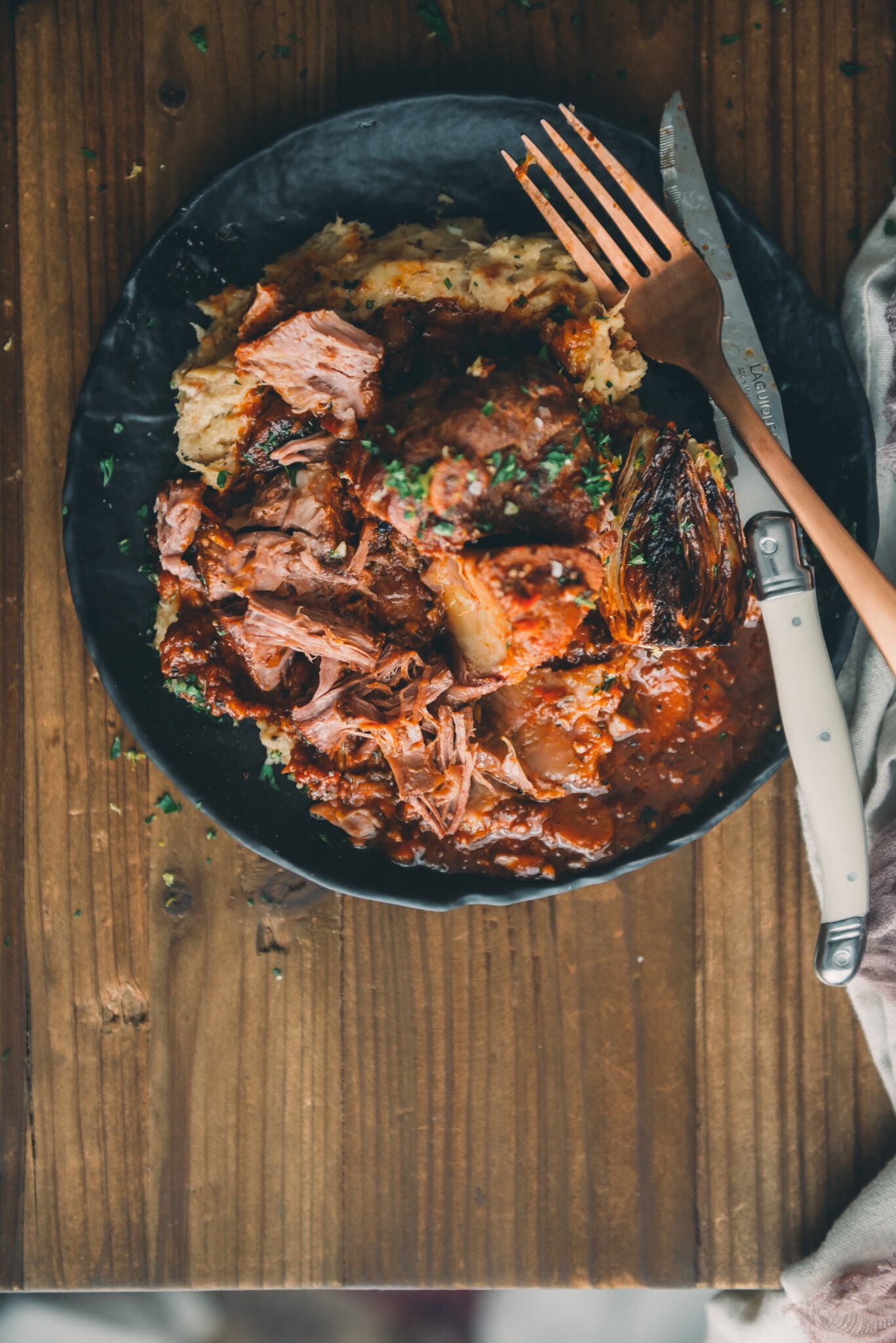 Plate of osso buco removed from the bone into tender shredded pieces with sauce and mashed parsnips on wooden table