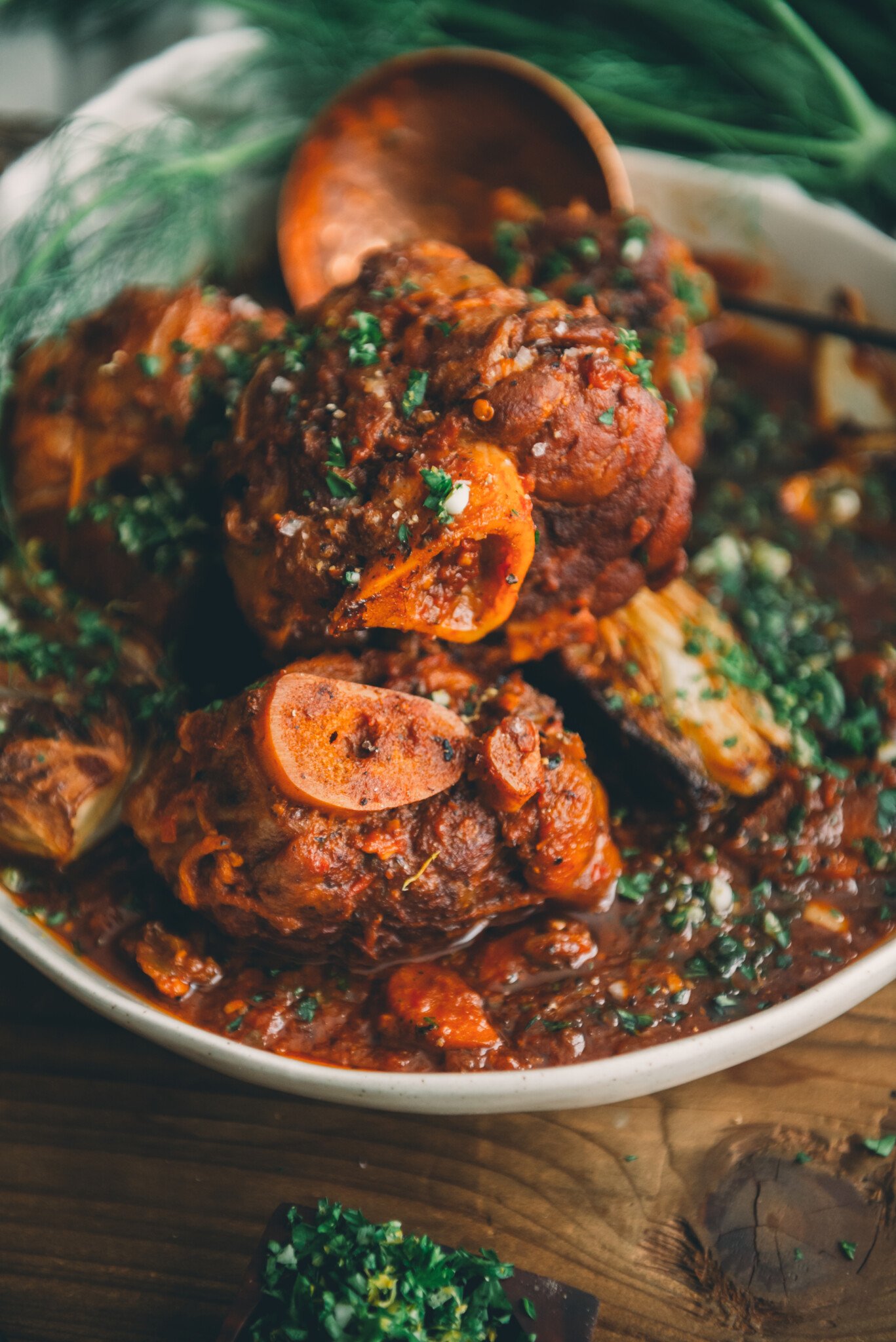 Close up of pork osso buco plated in a white dish with sauce and gremolata after 