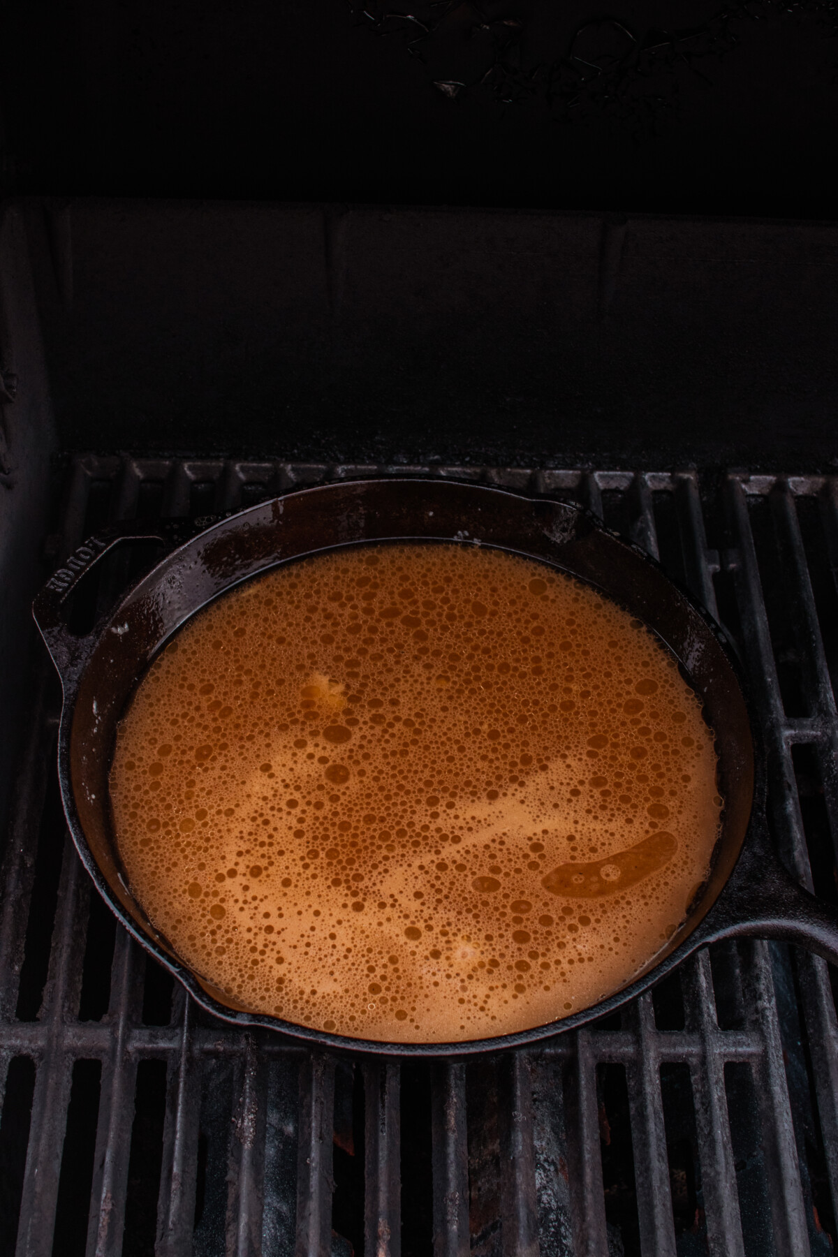Liquid added to roux in cast iron on grill.